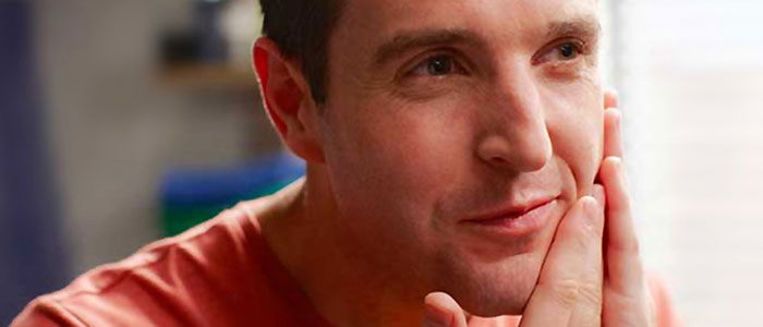 Zbliżenie na ogolonego mężczyznę, kt&oacute;ry dotyka swojej twarzy.