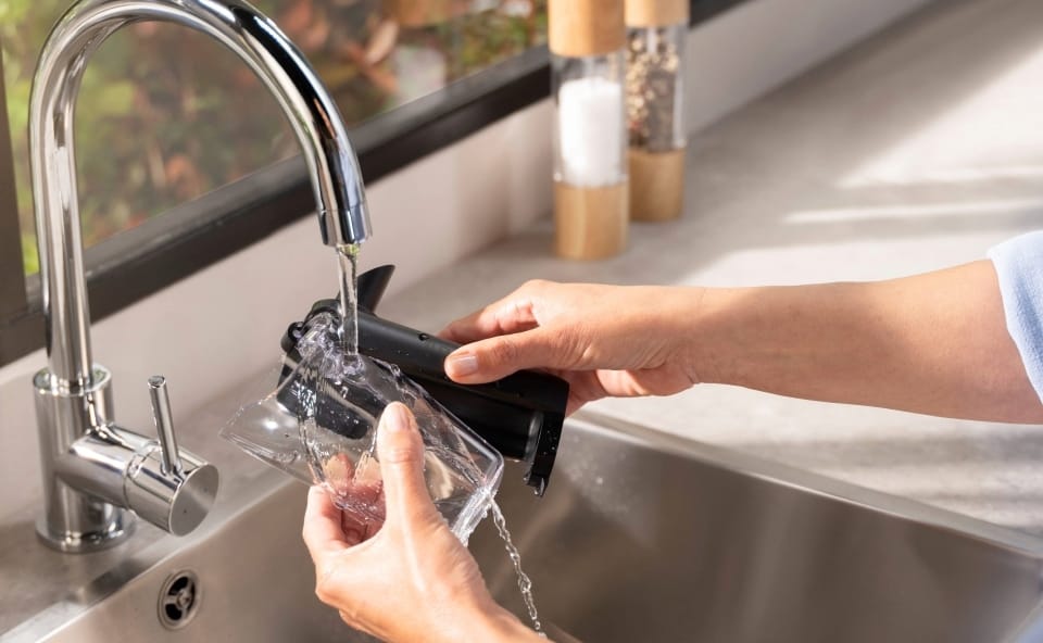 Kobieta myje w zlewie pojemnik na mleko od ekspresu do kawy.