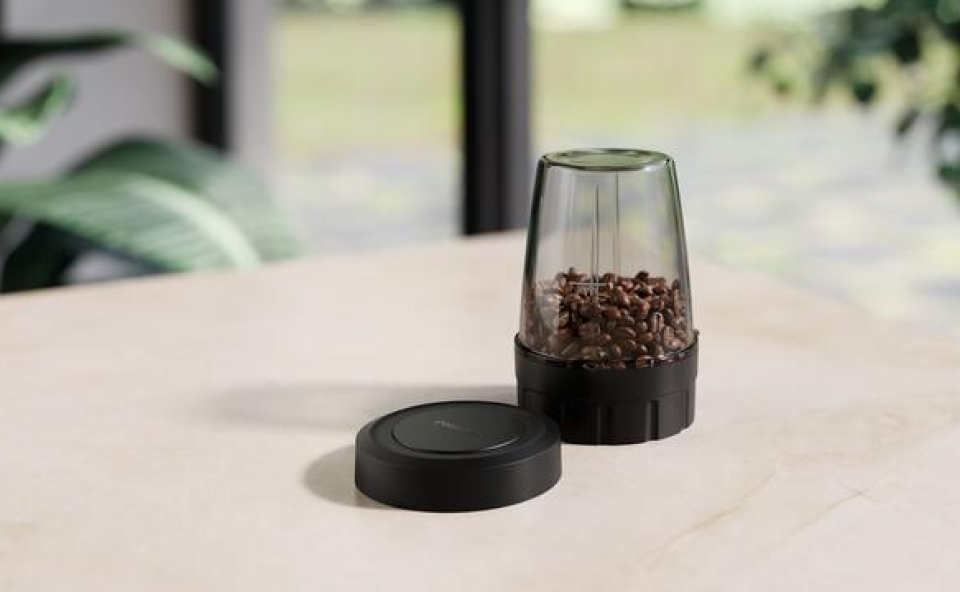Młynek do kawy, wypełniony kawą ziarnistą, postawiony na stole.