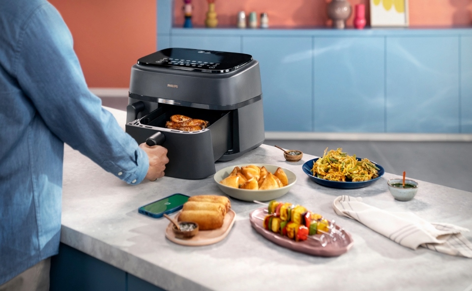 Mężczyzna wyciąga jedną z dw&oacute;ch szuflad frytkownicy beztłuszczowej, żeby sprawdzić czy danie jest gotowe.