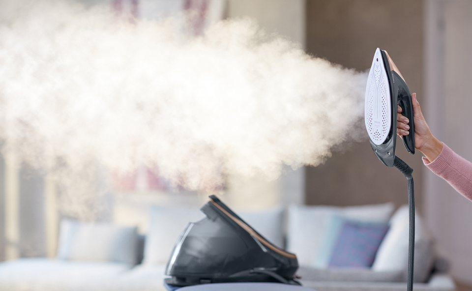 Kobieta trzyma w ręku żelazko parowe i pokazuje jego działanie