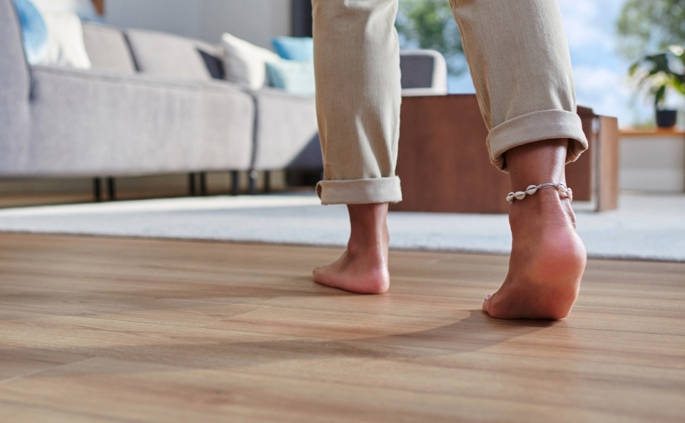 Kobieta idzie boso po czystej podłodze umytej przez robota sprzątająco-mopującego.