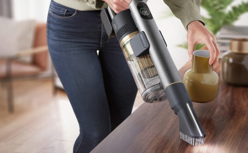 Kobieta sprząta szafkę z kurzu ręcznym odkurzaczem bezprzewodowym.