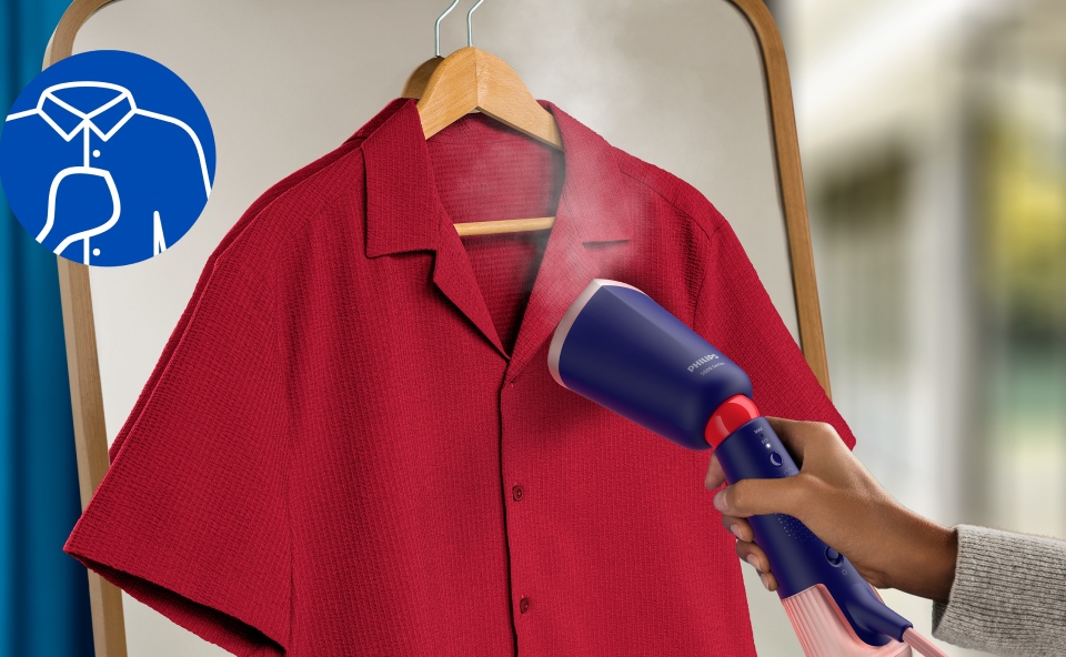 Kobieta prasuje czerwoną koszulę polo używając parownicy.