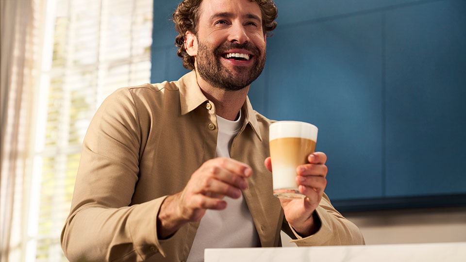 Mężczyzna siedzi na kanapie, słucha muzyki i popija dopiero co zaparzoną w ekspresie czarną kawę.