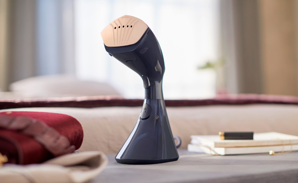 Czarna parownica stoi na stoliczku w salonie, obok wyprasowane ubrania.