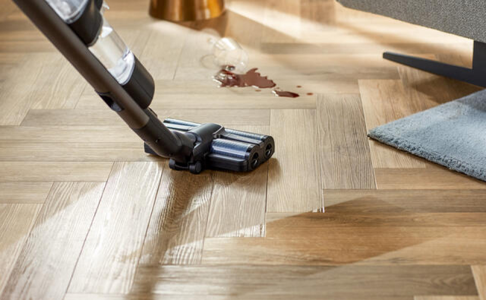 Mężczyzna sprząta rozlaną kawę z drewnianej podłogi odkurzaczem myjącym