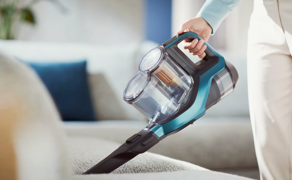 Niebieski ręczny odkurzacz czyszczący tapicerowaną szarą kanapę