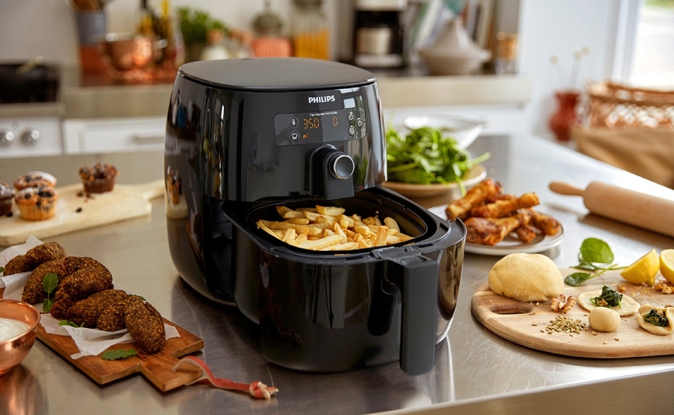 Czarny air fryer przygotowuje zdrowe frytki, obok niego leży reszta przygotowanych już dań.