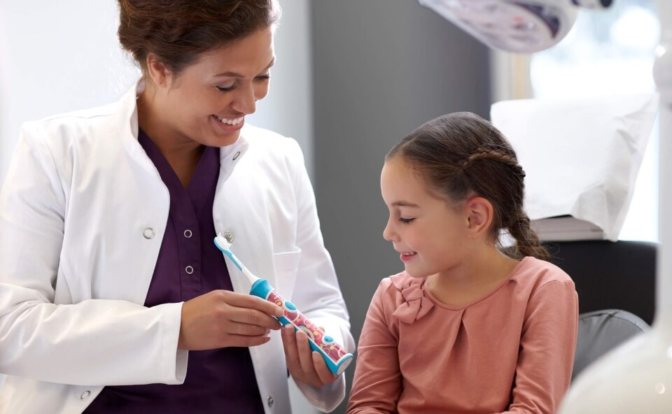 Uśmiechnięta dentystka wręcza dziewczynce szczoteczkę Philips Sonicare.