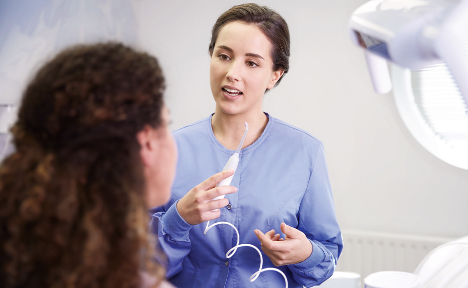 Higienistka stomatologiczna instruująca pacjenta jak używać irygatora do zęb&oacute;w.