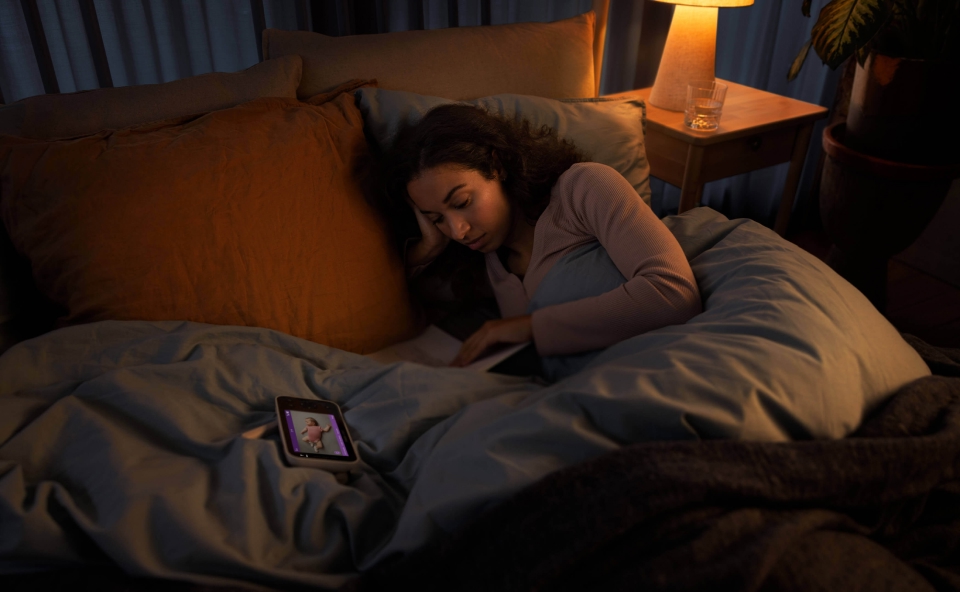 Kobieta leży w łóżku, patrząc na ekran smartfona, który wyświetla obraz z elektronicznej niani.