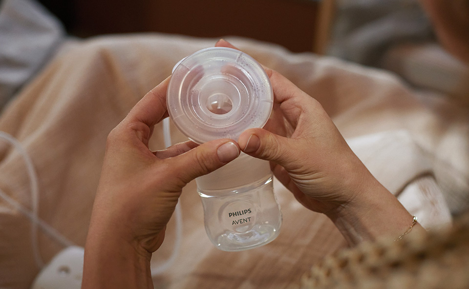 Kobieta używająca elektrycznego laktatora do odciągania mleka, siedzi wygodnie, trzymając urządzenie przy piersi.