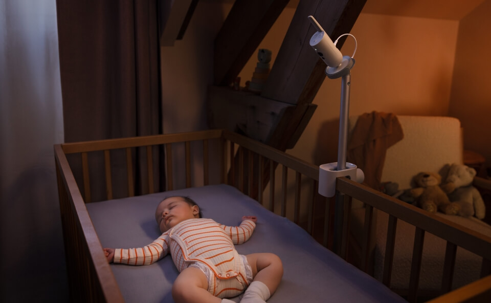 Śpiące dziecko w ł&oacute;żeczku monitorowane przez kamerę wideo umieszczoną na specjalnym uchwycie obok ł&oacute;żeczka.