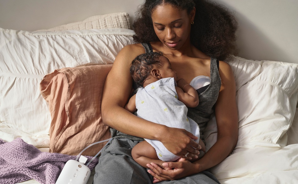 Kobieta leżąca na ł&oacute;żku z niemowlakiem, używająca laktatora Phiilips Avent Hands Free