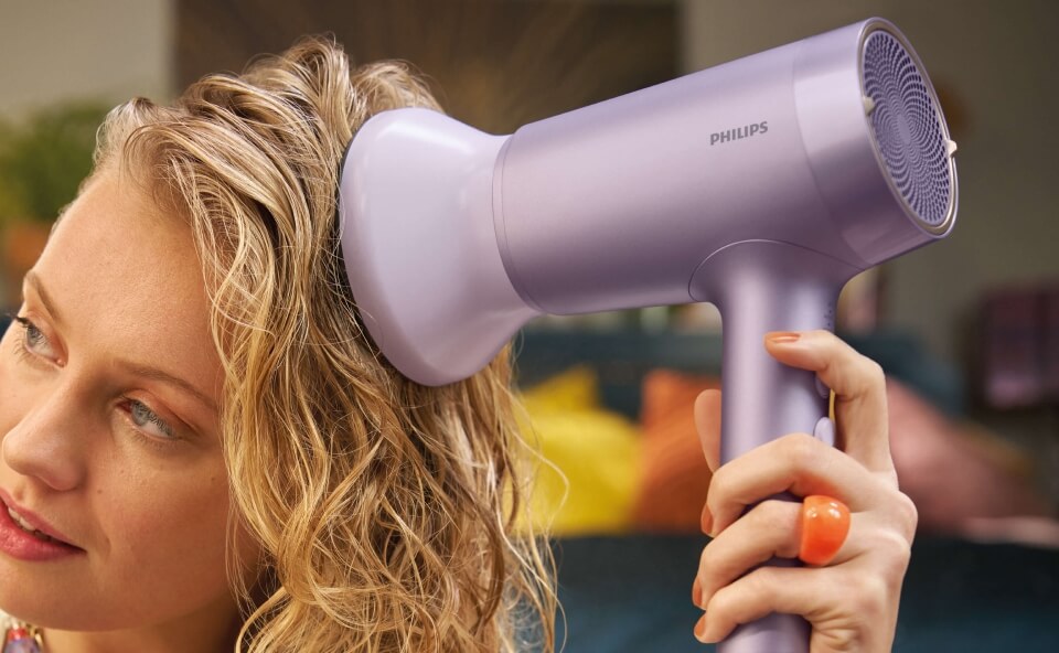 A woman using a purple Philips hair dryer with a diffuser attachment to dry her curly hair.