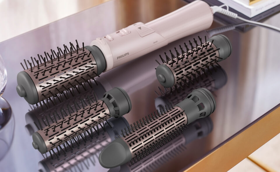Suszarko-lokówka marki Philips z kilkoma wymiennymi nasadkami w różnych rozmiarach, umieszczona na lśniącej powierzchni stołu. Nasadki szczotkowe mają plastikowe kolce i różnią się wielkością, co sugeruje różne zastosowania do stylizacji włosów.