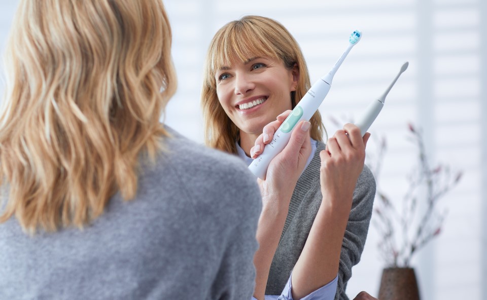 kobieta myje zeby przed lustrem w dloni trzyma szczoteczke soniczną philips