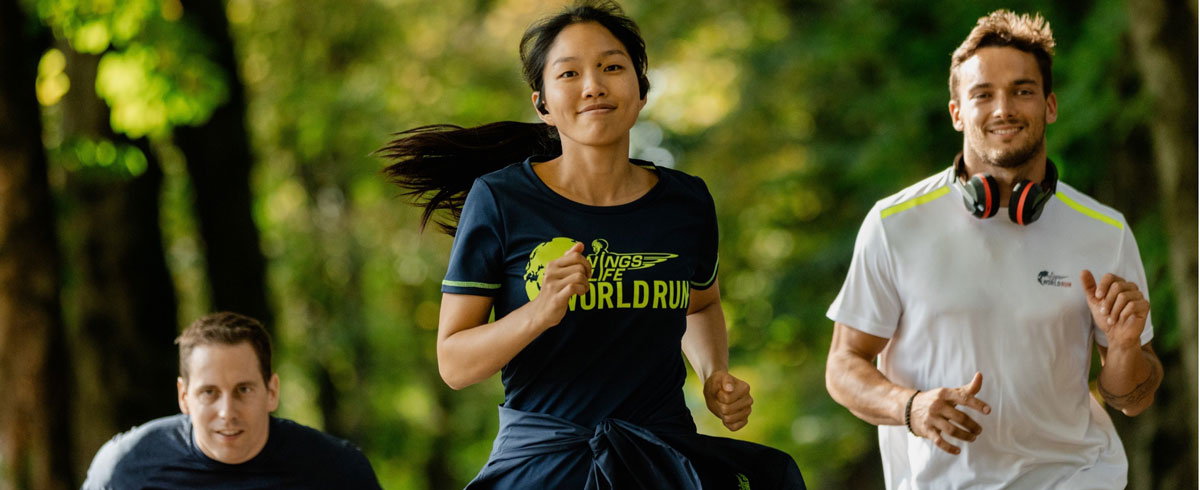 Radośnie biegnący trzej uczestnicy światowego biegu Wings for Life World Run z założonymi słuchawkami sportowymi Philips.
