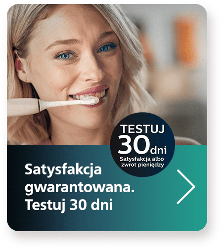 Grafika promująca 30-dniowy okres testowy szczoteczki do zęb&oacute;w. Na obrazie znajduje się młoda kobieta z jasnymi włosami, kt&oacute;ra używa białej szczoteczki do zęb&oacute;w. Tekst na grafice głosi: "Satysfakcja gwarantowana. Testuj 30 dni" oraz "Satysfakcja albo zwrot pieniędzy". W dolnej części znajduje się zielona strzałka wskazująca na możliwość przejścia do dalszych informacji.